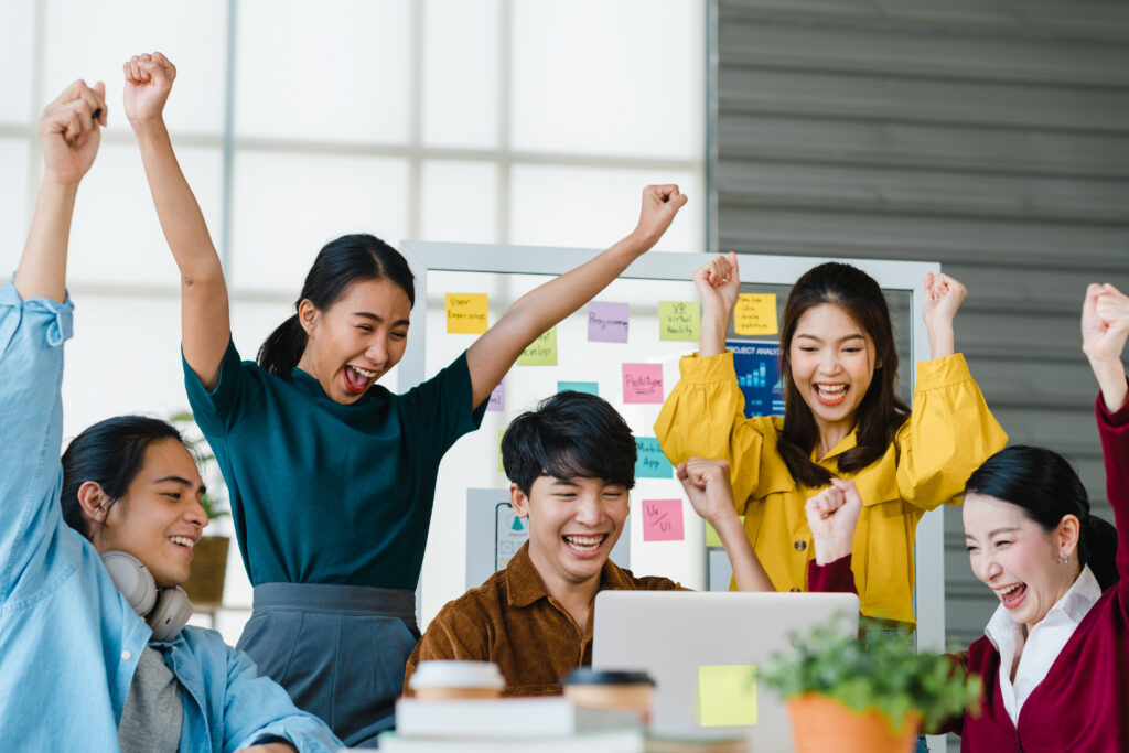 A group of young professionals dressed in smart casual attire, discussing business, exchanging high-fives, and signing an agreement in an office setting, representing the concept of working smart with coworkers.